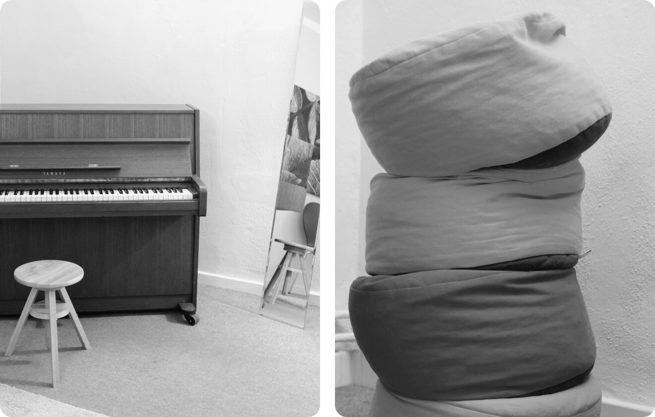 Raum mit Klavier, Spiegel, Hocker und gestapelten Meditationskissen.